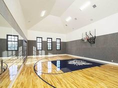 an indoor basketball court with hard wood floors and white walls, surrounded by black framed windows