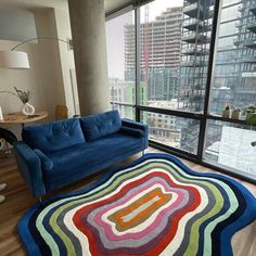 a living room with a blue couch and rug in front of large windows overlooking the city