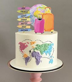 a white cake with colorful decorations and luggage signs on the top, sitting on a pink pedestal