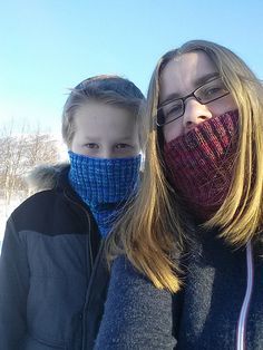 two people standing next to each other in the snow wearing knitted face coverings