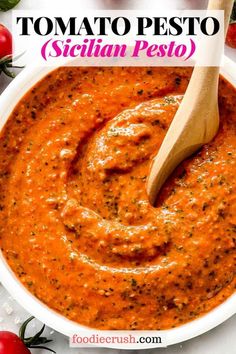 Tomato Pesto (Sicilian Pesto) | foodiecrush.com Image shows a closeup overhead shot of a white bowl filled with a creamy cherry tomato pesto, with a wooden spoon resting in the bowl and cherry tomatoes shown in the foreground and background