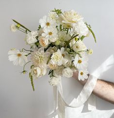 a bouquet of white flowers is being held by a man's arm with a ribbon around it