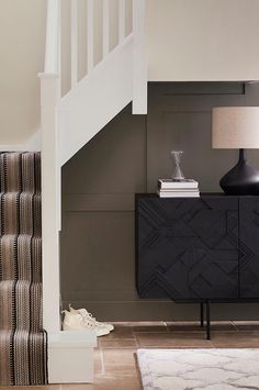 a black cabinet sitting under a stair case next to a white bannister with a lamp on top