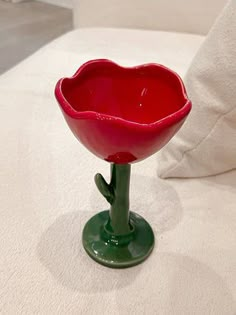 a red flower shaped bowl sitting on top of a white bed next to a pillow