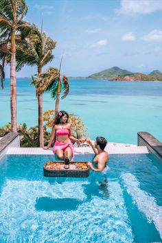 two people in a swimming pool with palm trees and the ocean in the back ground