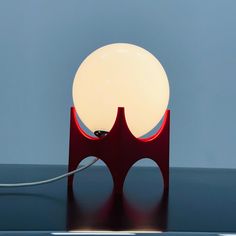 a red table lamp sitting on top of a black table next to a blue wall