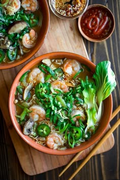 two bowls of shrimp and vegetable soup with chopsticks next to it on a cutting board