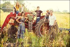 a group of people sitting on top of an old tractor in a field with tall grass