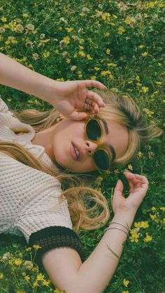 a woman laying in the grass with her hands on her head and sunglasses over her eyes