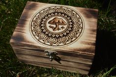 a wooden box with an intricate design on the lid sits in the middle of some grass