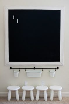 three white stools are in front of a chalkboard