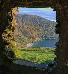 an open window in the side of a stone wall looking at a lake and mountains