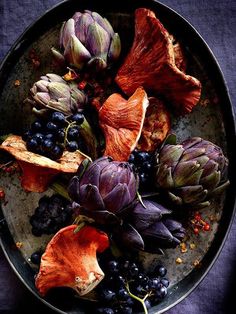 artichokes, grapes and other vegetables are on a plate with purple linen