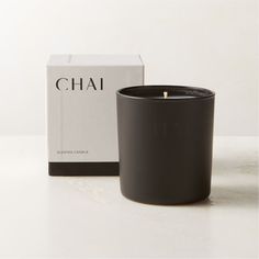 a black candle sitting next to a box on a white counter top with the word chai written in it