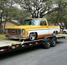 an orange and white truck is on the back of a flatbed trailer with trees in the background