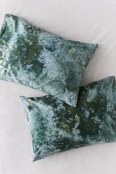 two green pillows sitting on top of a bed next to each other with white sheets