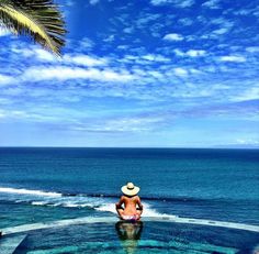 a person sitting on the edge of a swimming pool with a view of the ocean