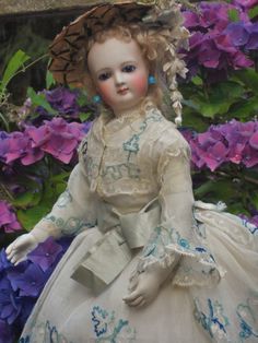 a doll is sitting in front of some purple flowers and wearing a dress with blue trim