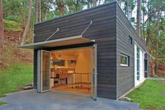 an open garage door on the side of a small house in the middle of a forest