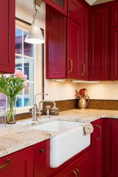 a kitchen with red cabinets and marble counter tops, an island style sink in the center