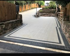 an empty driveway in the middle of a residential area with stone walls and brick walkways