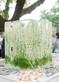 an ice block with flowers and seaweed in it on a table at a wedding