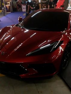 a red sports car parked in a showroom with people looking at the cars on display