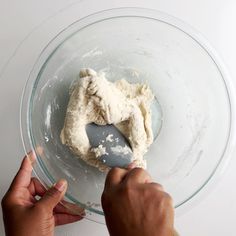 someone mixing dough in a glass bowl with a plastic spatula on the counter top