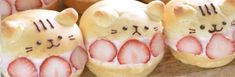 some very cute looking bread shaped like cats with strawberries in their mouths and eyes