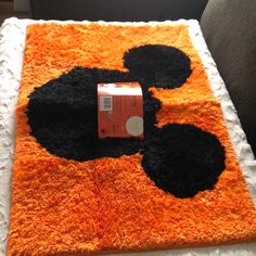 an orange and black rug with mickey mouse design on the floor next to a can of soda