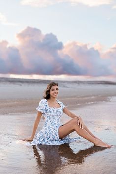 a woman is sitting on the beach with her feet in the water and she is smiling