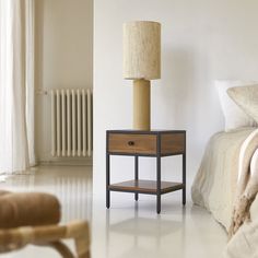 a nightstand with a lamp on it next to a bed in a white walled room