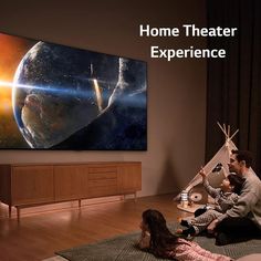 two people sitting on the floor in front of a large screen tv with an image of space