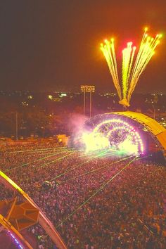 an aerial view of a concert at night with fireworks in the air and people watching