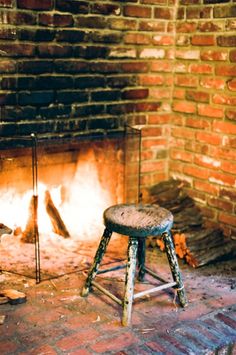 an old stool sitting in front of a fire place with logs on the floor and brick walls