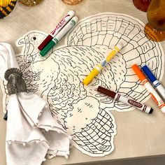 a turkey shaped paper plate with markers and markers on it next to some wine glasses