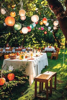 an outdoor dinner table with paper lanterns strung from the tree and on the ground,