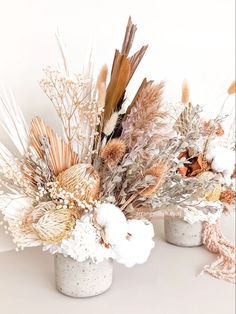 two vases filled with dried flowers on top of a white tablecloth covered surface