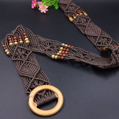 a brown belt with wooden beads and a gold ring on the end, sitting next to a flower