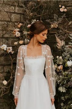 a woman standing in front of a brick wall wearing a wedding dress with sheer sleeves