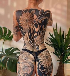 a woman with tattoos on her back standing next to a potted plant