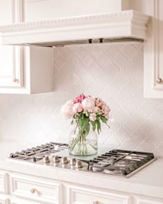 a vase with flowers on top of a stove in a white kitchen countertop next to cabinets