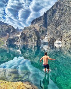 a man standing in the water with his arms spread out, looking at mountains and blue sky