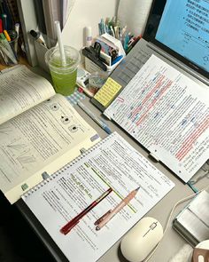 a laptop computer sitting on top of a desk next to papers and a cup filled with liquid