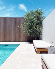 an empty pool next to a wooden fence with a tree in the middle and two lounge chairs near it