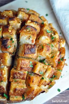 a white plate topped with tofu and cheese covered in parmesan sauce, garnished with green herbs