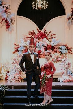 a man and woman standing next to each other in front of a decorated stage with flowers