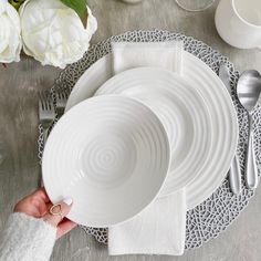 a person holding a white plate on top of a table next to silverware and flowers