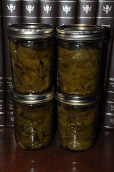 four jars filled with pickles sitting on top of a table next to some books