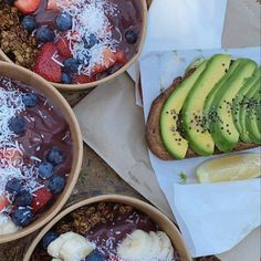 three bowls filled with fruit and granola next to a sandwich on top of paper